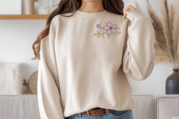 Etsy embroidery designs on a beige sweatshirt featuring a small pink flower with green leaves on the chest